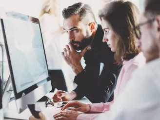 Three colleagues reviewing on-screen content at PC